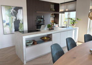 Luxe design keuken met kookeiland mat wit, wit grijs marmerlook aanrechtblad en achterwand + donkere houtlook kastenwand met koffiehoek