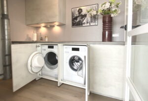 Droger en wasmachine achter deur in keukenkast en onder een werkblad in de (bij)keuken