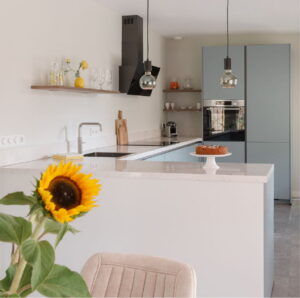 Moderne U-keuken ijsblauw met bar, RVS Quooker en spoelbak, oven met RVS frame, hoogglans wit composiet werkblad en glazen hanglampjes - I-Kook keuken van een trotse klant Moderne U-keuken ijsblauw met bar, RVS Quooker en spoelbak, oven met RVS frame, hoogglans wit composiet werkblad en glazen hanglampjes - I-Kook keuken van een trotse klant